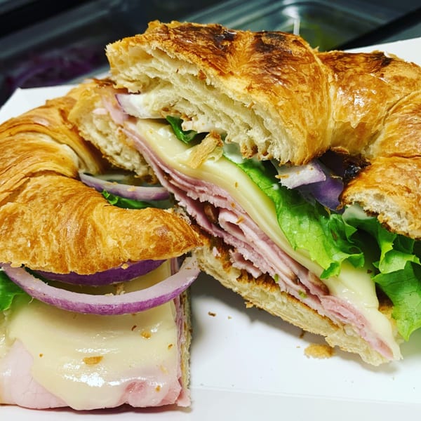 A croissant sandwich with ham, melted cheese, red onion, and lettuce, cut in half.
