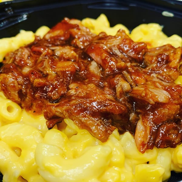 Close-up of macaroni and cheese topped with savory pulled pork in a dark bowl.